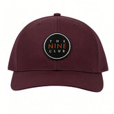 OG Logo Maroon Patch Trucker Hat, all-maroon trucker with black round The Nine Club patch, front view